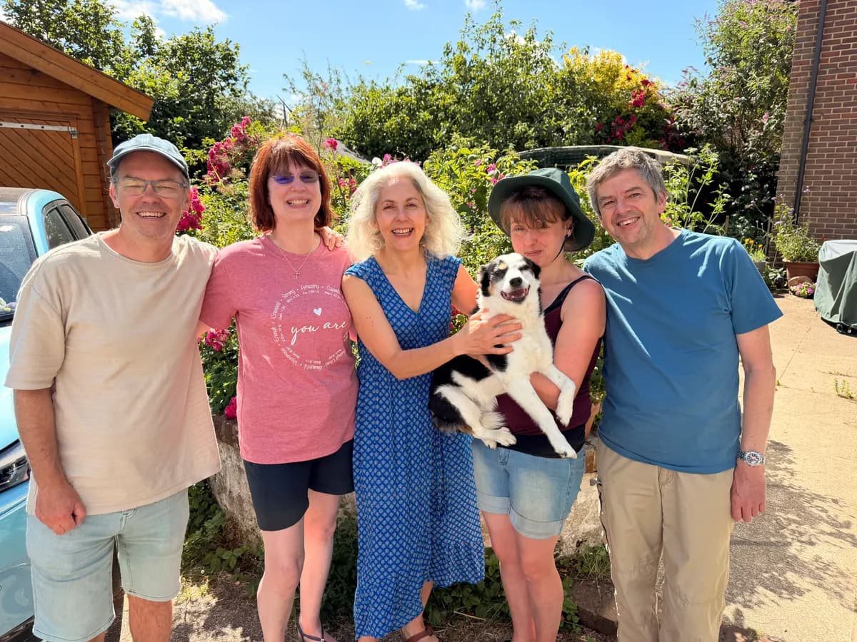 Five friends and a collie dog smiling together in a sunny garden